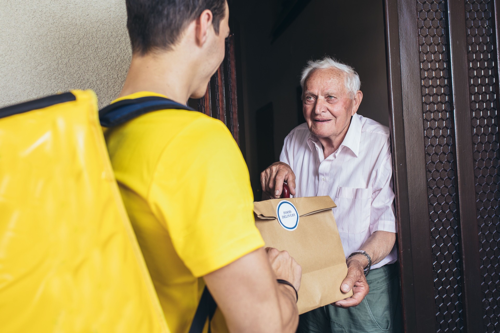 Young male volunteer delivering shopping to senior man.